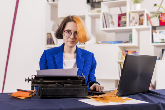 Young Girl, Office Worker, Works On Old Typewriter And Modern Laptop At Same Time. Look At Camera.