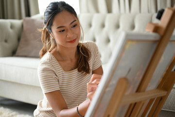 An attractive Asian female artist painting picture on canvas easel