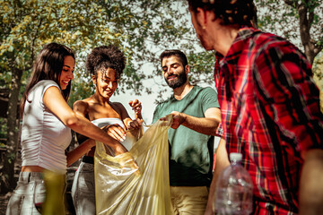 Group of young people collecting trash for recycling in the wilderness - multiethnic friends after picnic limiting their  environmental footprint