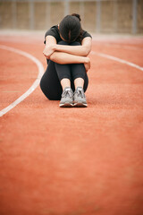 Today has been tough. Shot of a young woman looking upset while sitting on the track.