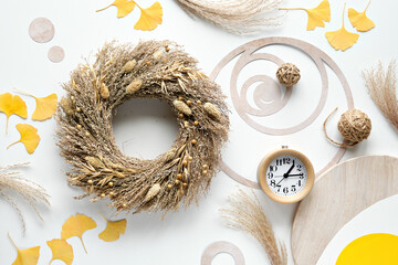 Autumn time background. Dry grass wreath, wood alarm clock, off white table with ginko leaves,...