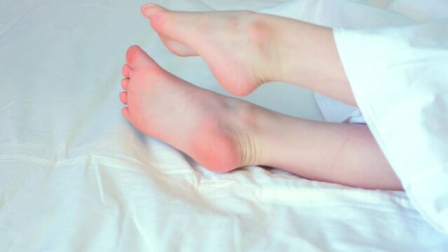 Bare feet of a child on white, morning kid stretches lazily, side view.