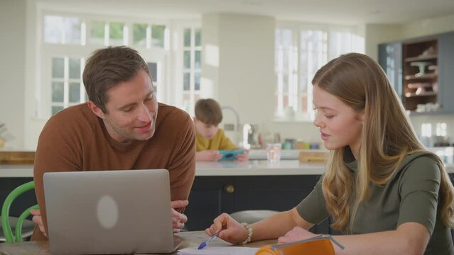 Parents helping teenage daughter with homework sitting at kitchen table at home using laptop - shot in slow motion