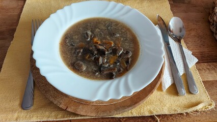 Pilzsuppe in einem weißen Teller. Porzellan platte auf einem Holztablett. Gelbe Tischdecke auf einem Holztisch. Weiße Serviette. Besteck auf einem Teller. Vegetarisches Gericht. Leichtes Mittagessen.