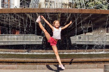 Acrobatic exercise girl smiling. Teen girl have fun in street fountain at hot sunny day. Child city fountain. 