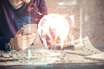 Double exposure of man's hands holding and using a digital device and bulb hologram drawing. Idea concept.