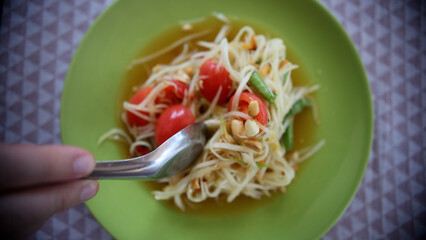 Close up of fresh yummy delicious Thai traditional popular street food spicy green papaya salad or Som Tam in green dish