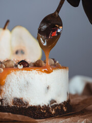 Confectioner pours liquid caramel on pear cheesecake with spoon