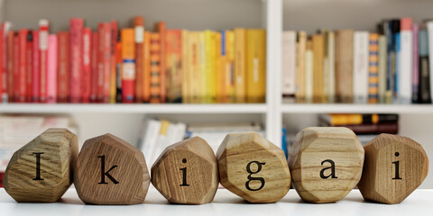 Ikigai word (Japanese word for reason for being) written on wooden blocks. Blurred books behind. Life meaning concept.