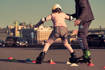 A child learns to roller skate with a trainer outdoors. The girl performs tricks on roller skates....