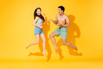 Fototapeta na wymiar Summer portrait of fun energetic Asian couple jumping in isolated yellow color background