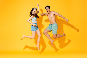 Summer portrait of fun energetic Asian couple jumping in isolated yellow color background