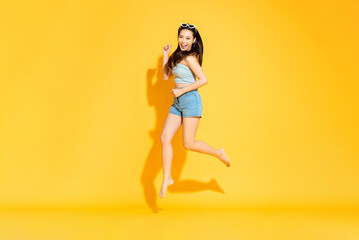 Fototapeta na wymiar Pretty Asian woman in summer outfit smilng and jumping in studio isolated yellow color background