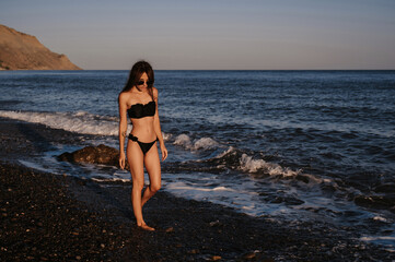 happy young girl with a sexy body in a swimsuit and sunglasses is relaxing on the beach by the sea in summer