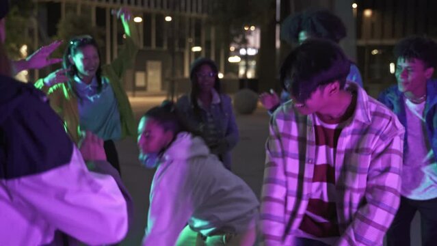 Group of trendy young diverse teenager Asian American friends having fun dancing in music street party in the city at night