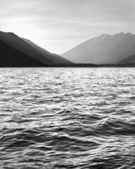 Vertical shot of the seascape waves against mountains in grayscale
