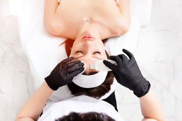 Ultrasound facial peeling. Ultrasonic facial cleansing at cosmetology clinic. Cosmetologist with...