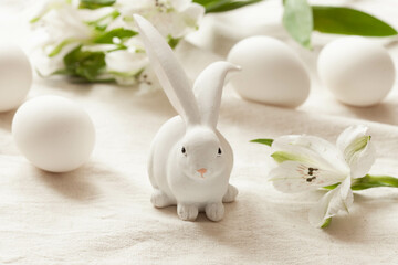 White easter rabbit, white flowers and white eggs on light rustic background, close-up