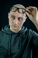 Portrait of a bald young man holding black eyeglasses on his forehead while looking at something to the side