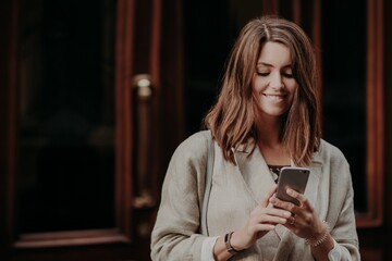 Woman shares multimedia files via cell phone, dressed in elegant clothes, reads positive news in internet website, connected to wireless internet