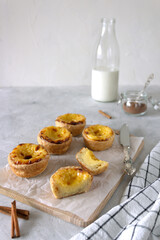 Portuguese custard tart served with milk and cinnamon. Egg tarts on the wooden board with a silver knife and cinnamon sticks beside.