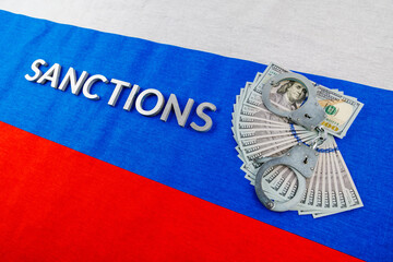 the word sanctions laid with silver metal letters on russian tricolor flag near dollar banknotes...