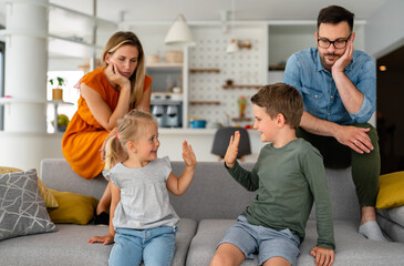 Tired parents sitting on couch feels annoyed exhausted while happy children playing together.