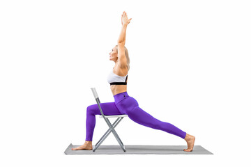 Iyengar yoga. Fit caucasian woman in purple leggings practice warrior pose using a chair, isolated on white.