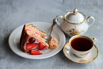 Birthday cake on a plate. Close up photo of strawberry cake and cup of tea on light grey...