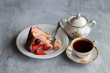 Piece of strawberry cake and cup of black tea on a table. Light grey background with copy space. Sweet food close up. 
