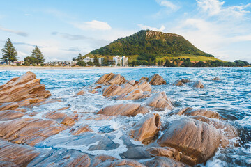Beautiful view of rocky seashore with mount Maunganui in the background in New Zealand