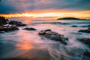 Scenic view of the rocks on a sandy beach at the sunset under the cloudy sky, shot in long exposure
