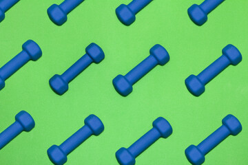 Rows of blue dumbbells on bright green gym mat 