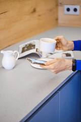 Hands of woman holding cup of coffee and smartphone