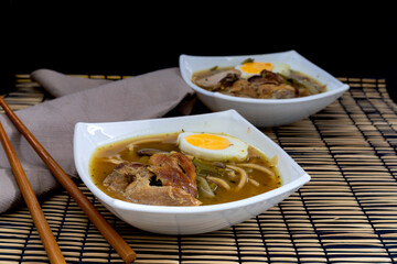 Individual bowls of Ramen, oriental soup on black background with bamboo tablecloth