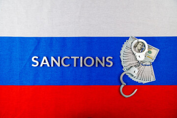 the word sanctions laid with silver metal letters on russian tricolor flag near dollar banknotes...
