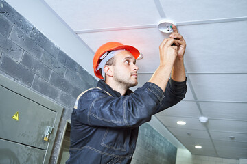worker installing smoke detector on the ceiling. Fire alarm system installation - obrazy, fototapety, plakaty
