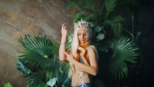myth Nagga woman dancing with white milk Boa constrictor albino snake. Fantasy asp girl queen. Serpent crawls over body neck. Silver costume body tail Lady viper dancer. Backdrop studio green palants