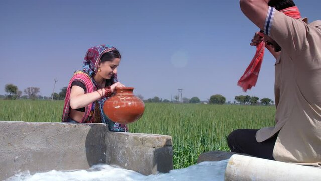 Attractive village lady filling up water for daily use in an earthen pot from a tubewell - freshwater  an Indian village scene. Married Indian couple from village sitting together in their rice fie...
