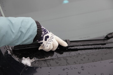 Woman's hands with warm gloves change the car wiper blade on the background of dark blue sky at winter evening, self seasonal car maintenance service