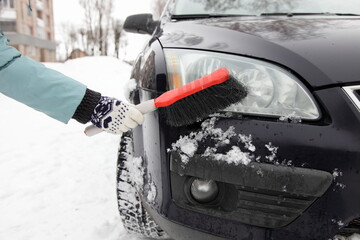 Woman's hand in a winter glove cleans the car headlight from snow with a brush in winter after snowfall in Europe © Ilya