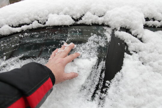 Frosted car side door window cleaning from a hoar frost before a drive with a naked hand without brush at frozen winter day  after snofall in Europe