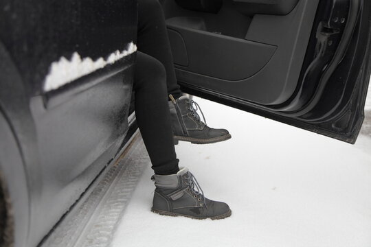Women's legs in warm clothes get out of the car on a snowy road on a winter day after a snowfall in Europe