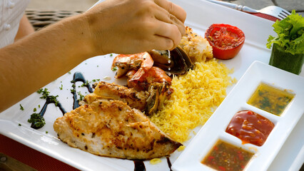 Chef hand squeeze lemon juice to seafood platter with charcoal grilled shrimps, mussels and fish fillet with fried rice. Unrecognizable female hand prepare dish with prawns squeezing citrus to plate.