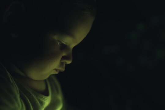 Side portrait of a focused toddler over dark, black background. Indoor shot. High quality photo