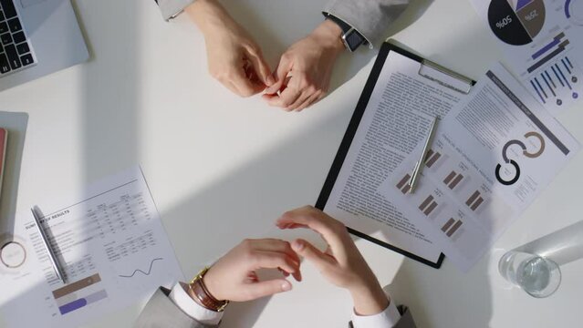 Top Down Shot Of Two Businessmen In Formalwear Sitting At Office Table With Documents On It, Shaking Hands And Discussing Work