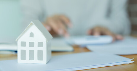 close up home model with young woman hand check summary of refinance expense on book for planning...