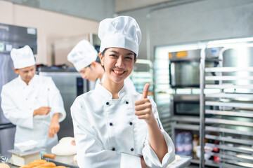 Smiling  asian  female bakers looking at camera..Chefs  baker in a chef dress and hat, cooking together in kitchen.Team of professional cooks in uniform preparing meals   in the kitchen.