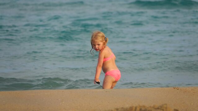 The little cute girl in swimsuit is playing with the swimming board on the beach