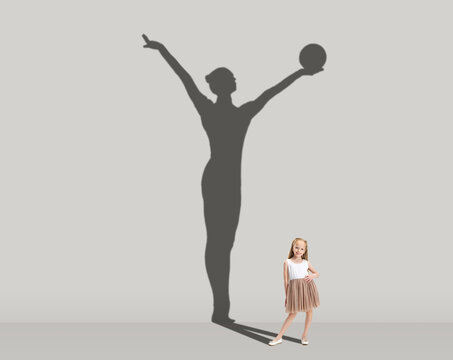 Kids and future. Conceptual image with little girl dreaming about becoming gymnast isolated on studio gray wall. Focus on shadow